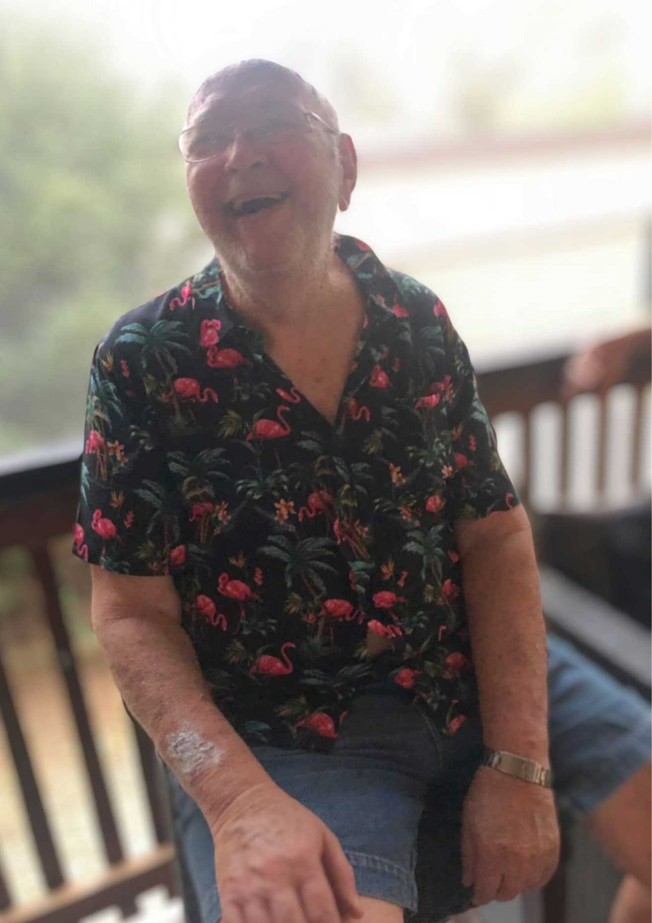 An elderly man sitting on a porch, smiling.